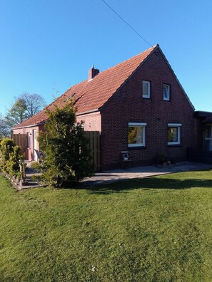 Une maison à deux étages, construite en briques, avec un toit recouvert de tuiles rouges, un petit porche et une pelouse bien entretenue.