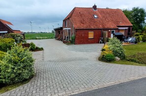 A residential area with a paved driveway leading to a brick house with a red-tiled roof.