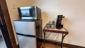 A compact kitchen with a refrigerator, microwave, and a small table with cups and a coffee maker. - Montana Magnificence Studio (Whitefish)