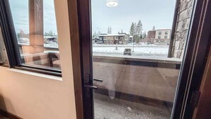 A room with a large window, a door, and a view of a snowy outdoor area with buildings. - Montana Magnificence Studio (Whitefish)