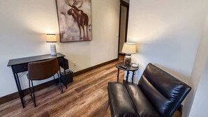 A room with a desk, chair, leather sofa, two lamps, and a moose painting on the wall. - Montana Magnificence Studio (Whitefish)
