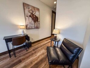 A room with a desk, chair, leather sofa, two lamps, and a moose painting on the wall. - Montana Magnificence Studio (Whitefish)