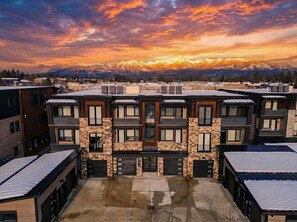 A multi-story residential building with a central courtyard, large windows, and a view of snow-capped mountains. - Montana Magnificence Chalet (Whitefish)