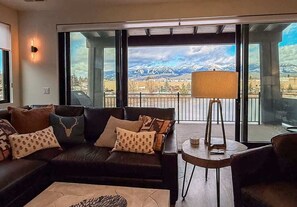 A modern living room with a large window, a sofa, a coffee table, and a lamp. - Montana Magnificence Chalet (Whitefish)