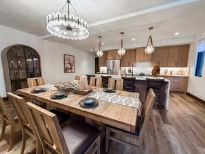 A modern kitchen with wooden cabinets, a central island, pendant lighting, and a dining area with a wooden table and chairs. - Montana Magnificence Chalet (Whitefish)