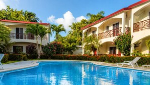 Une piscine entourée d’un bâtiment doté de balcons et agrémentée d’un aménagement paysager tropical.
