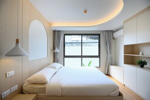 Ein modernes Hotelzimmer mit einem großen Bett, einem Nachttisch, einer Lampe, einem Fenster mit Vorhängen, einer Pflanze auf einem Regal und einer Klimaanlage.