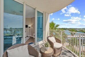 Ein Balkon mit Korbmöbeln, Blick auf einen Pool und eine Glastür zu einem Zimmer mit einem Bett und einer Lampe.