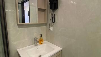 Un baño con lavamanos blanco, un espejo, un secador de pelo montado en la pared y una botella de jabón.