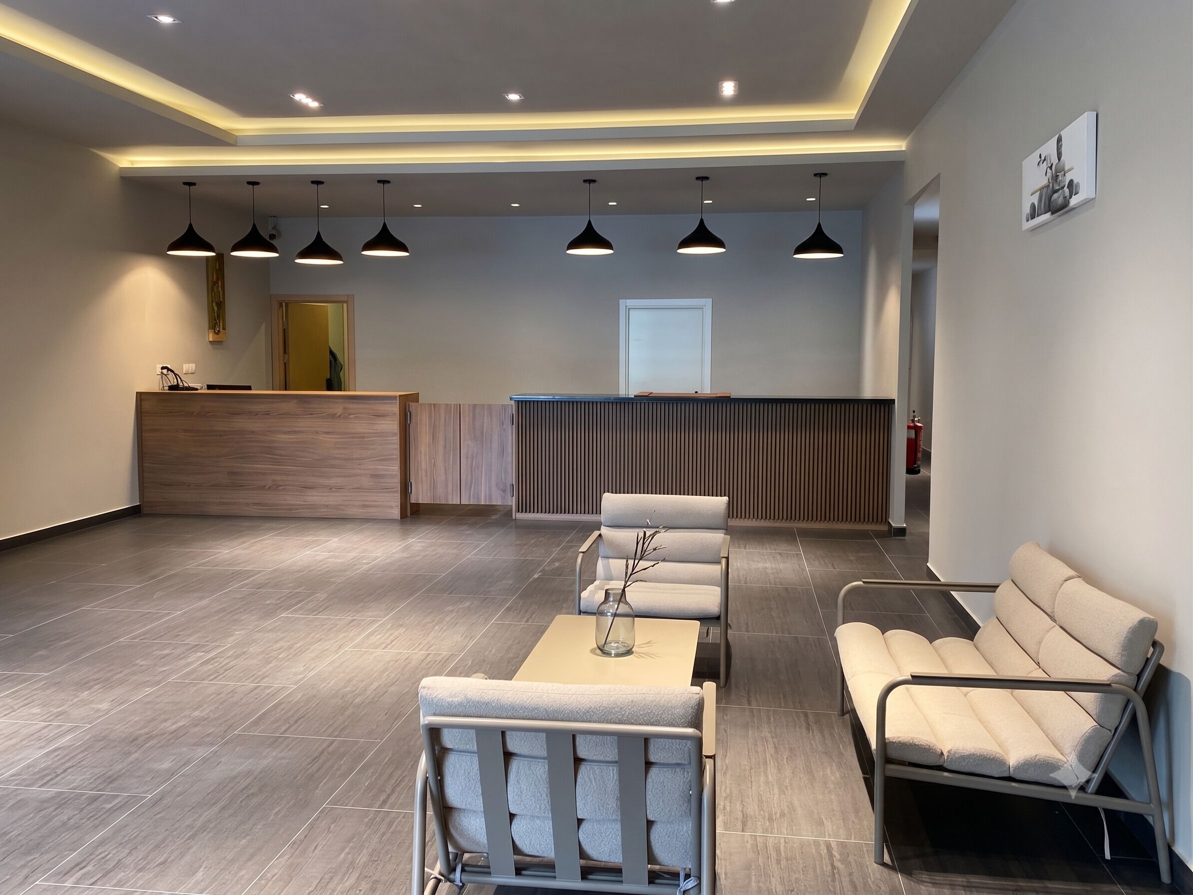 A reception area with a wooden reception desk, a waiting area with chairs and a sofa, and a fire extinguisher on the wall.