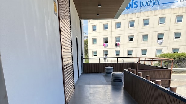 A covered outdoor area with a tiled floor, a wooden fence, and a building with windows in the background.
