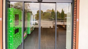 A modern building entrance with a glass door and a green patterned wall to the left.