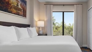 A hotel room with a large bed, a TV, a nightstand with a lamp, and a view of trees through the window. - 2-bedroom deluxe, full kitchen, resort Lake Buena Vista, Disney World - sleeps 6 (Lake Buena Vista)
