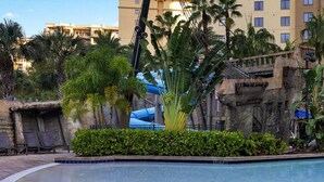 A pool area with a water slide, palm trees, and a building with balconies in the background. - 2-bedroom deluxe, full kitchen, resort Lake Buena Vista, Disney World - sleeps 6 (Lake Buena Vista)