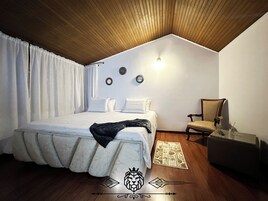 Un dormitorio con techo de madera, una cama con edredón blanco, una silla, una mesita y un aplique de pared.