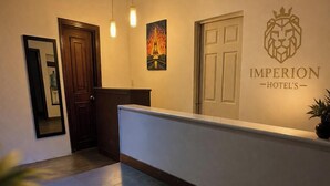 Uma área de recepção de hotel com balcão, uma porta, uma placa na parede e um quadro emoldurado.