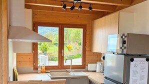 Una cocina moderna con vigas de madera, un refrigerador de acero inoxidable, lavavajillas y una ventana con vista a vegetación.
