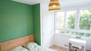 A bedroom with a bed, a desk, and a window with a view of trees. - Private Room in a Shared Apartment - Bron (Bron)