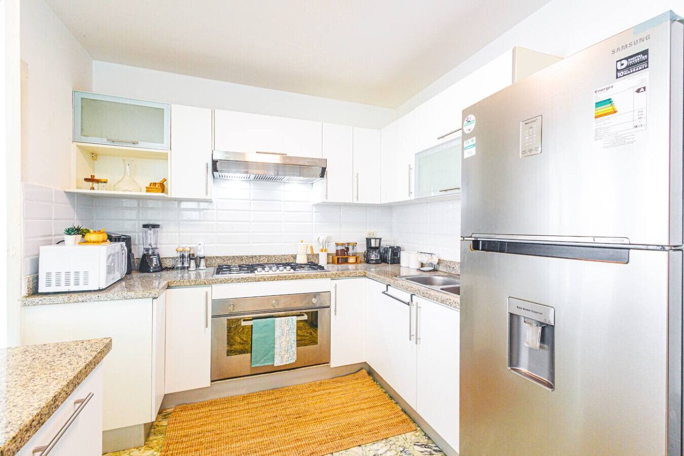 A compact kitchen with white cabinets, a stainless steel refrigerator, a built-in oven, and a microwave.