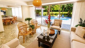 Un amplio salón con vista a la piscina, muebles de mimbre y una mesa de centro moderna.