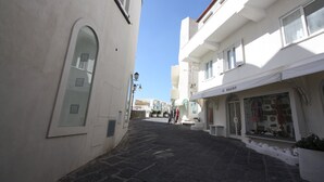 Una calle estrecha con edificios blancos, una tienda llamada 'IL RAGNO' y un suelo empedrado de piedra.