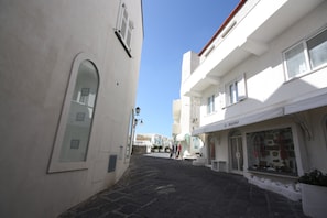 Une rue étroite bordée de bâtiments blancs, une boutique appelée « IL RAGNO » et un sol pavé de pierres.