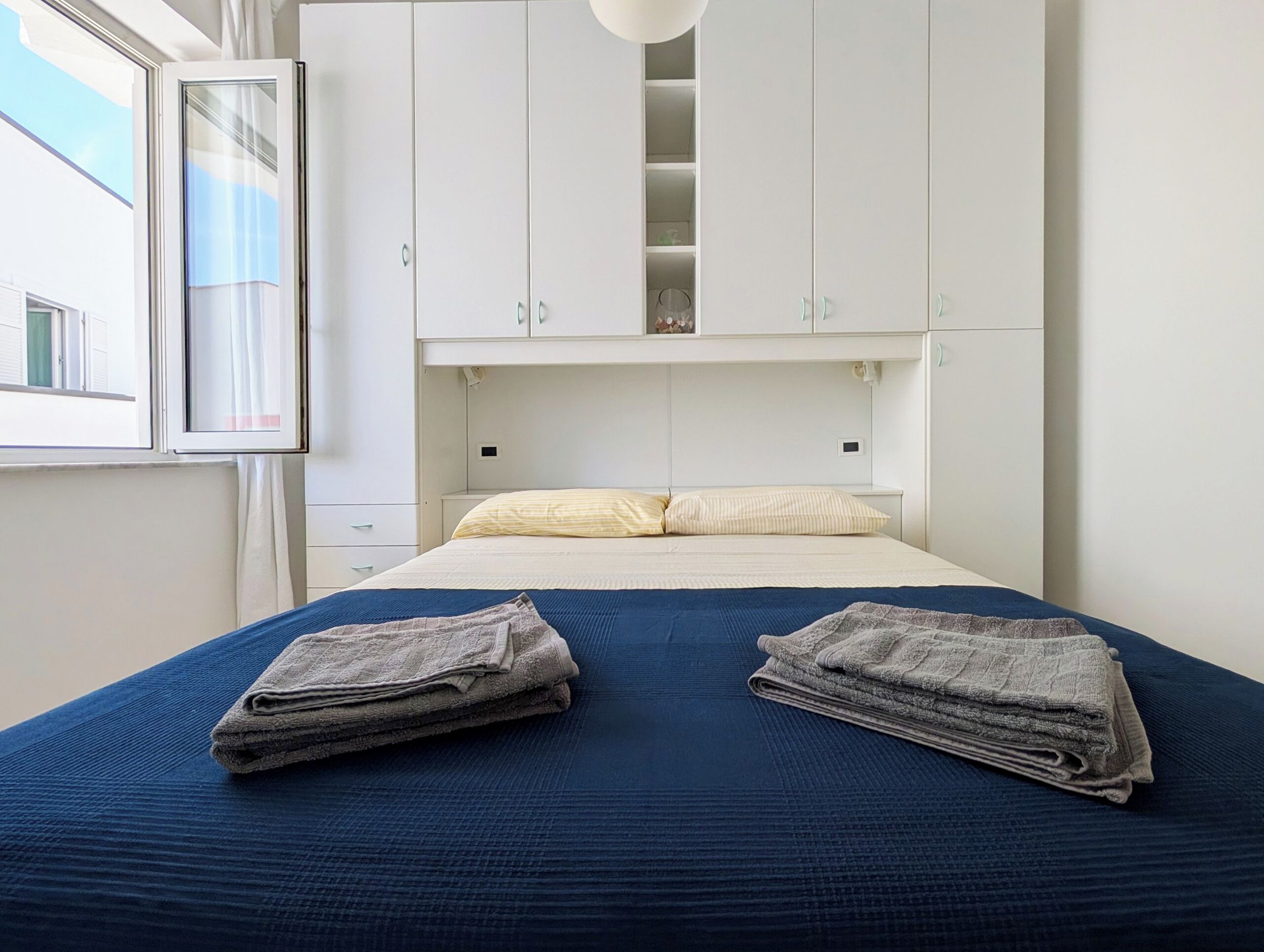 A bedroom with a bed, two side tables, a window, and white cabinets.