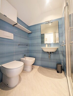 A modern bathroom with a bidet, toilet, and sink, featuring blue-tiled walls and a light wooden floor. - Santangiolese House - In the heart of Sant'Angelo (Sant'Angelo)