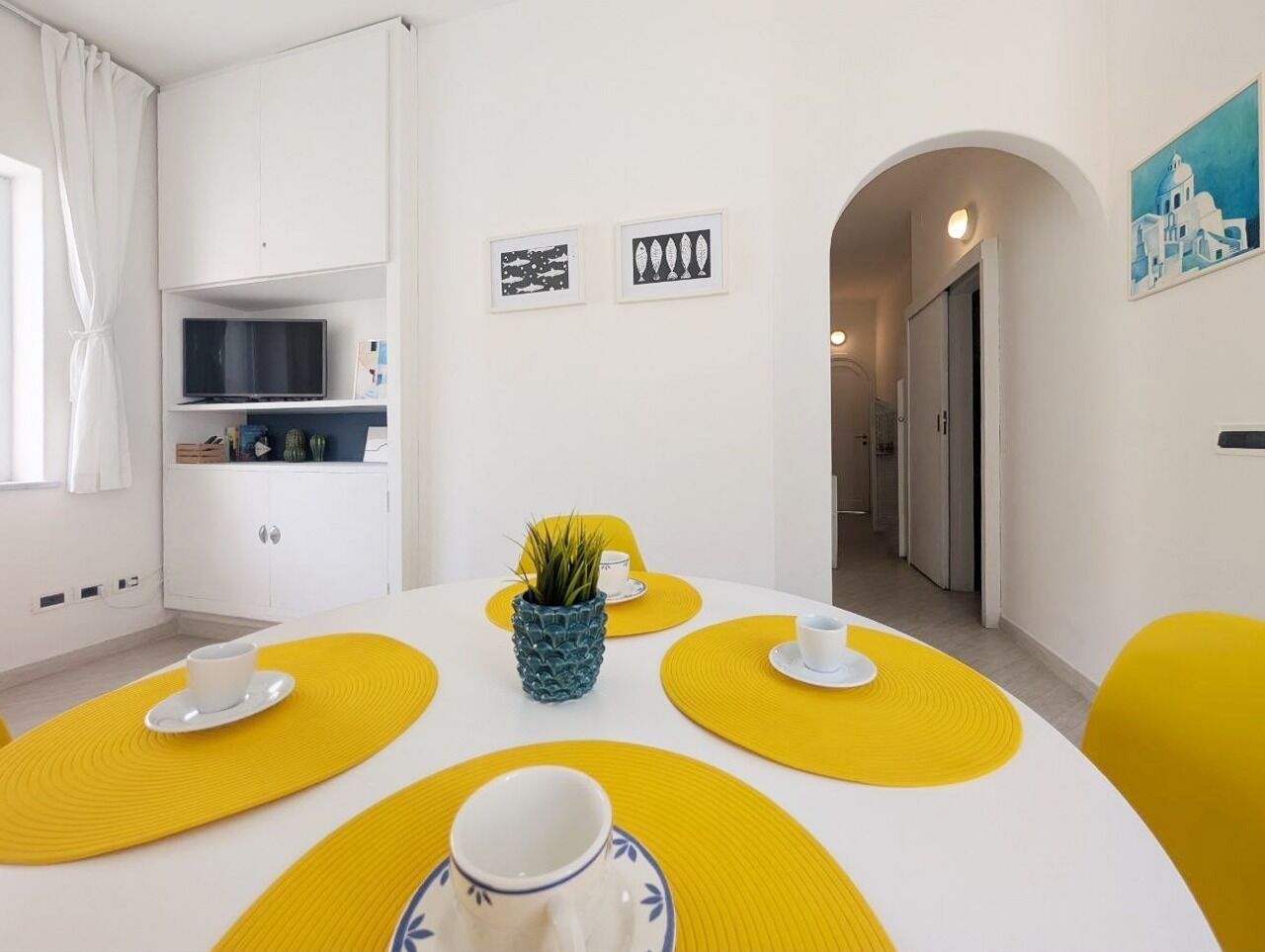 A dining area with a white table, yellow placemats, and a small potted plant.