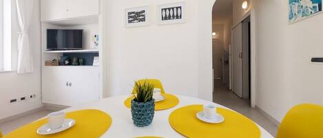 A dining area with a white table, yellow placemats, and a small potted plant.