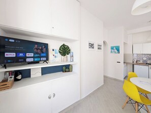 A modern room with a flat-screen TV, a dining area with yellow chairs, and a kitchen with white cabinets. - Santangiolese House - In the heart of Sant'Angelo (Sant'Angelo)
