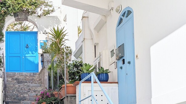 Un edificio blanco con una puerta azul y una escalera que sube a un segundo piso.