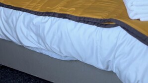 A neatly made bed with a white and gold bedspread, a wooden nightstand with a lamp, and a framed picture on the wall. - Eden homez (Bristol)