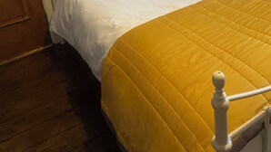 A bed with white bedding and a yellow quilt, a wooden door, a nightstand with a lamp, and a wall-mounted painting. - Eden homez (Bristol)