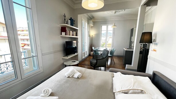A hotel room with a bed, a desk, a chair, a TV, and a balcony. - Balcon Palais Excelsior Grimaldi (Nice)