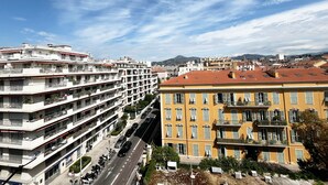 A multi-story building with balconies, a street in front, and a mountain in the background. - Balcon Palais Excelsior Grimaldi (Nice)