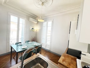 Uma sala de jantar com mesa posta para quatro pessoas, pia e vista para o exterior por grandes janelas.