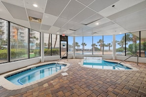 An indoor swimming pool with clear views of palm trees and a building outside. - A Coastal Paradise - Beachfront - Gym - Pool (Myrtle Beach)