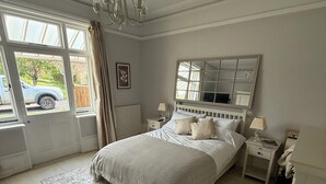 A bedroom with a large bed, a chandelier, a window with a view of a parked car, and a radiator. - Red House  (Guildford)