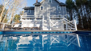 Une maison à deux étages avec une piscine, un espace salon extérieur et une terrasse en bois.