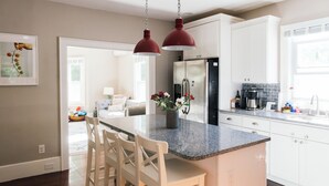 Une cuisine moderne avec des meubles blancs, un plan de travail en granit et un îlot central doté de tabourets de bar.
