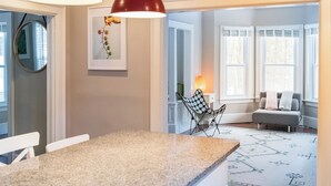Une cuisine dotée d’un plan de travail en granit, de luminaires suspendus rouges, d’un tableau encadré au mur et d’un coin repas avec une chaise et une table.