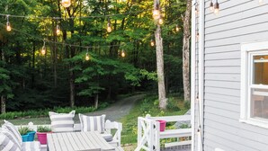 Une terrasse avec des sièges extérieurs et des guirlandes lumineuses, entourée d’une zone boisée.