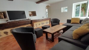 Una sala de estar con un sofá, sillas, un televisor y una pared de piedra.