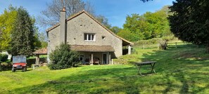 Ein Steinhaus mit Schornstein, einer überdachten Veranda und einem Picknicktisch in einem grünen Garten.