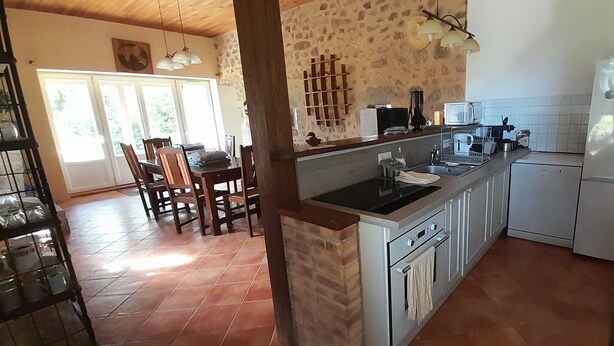Una cocina con pared de piedra, comedor con sillas, refrigerador y microondas.
