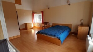 Un dormitorio con cama, cómoda, silla, ventana con cortinas y radiador.