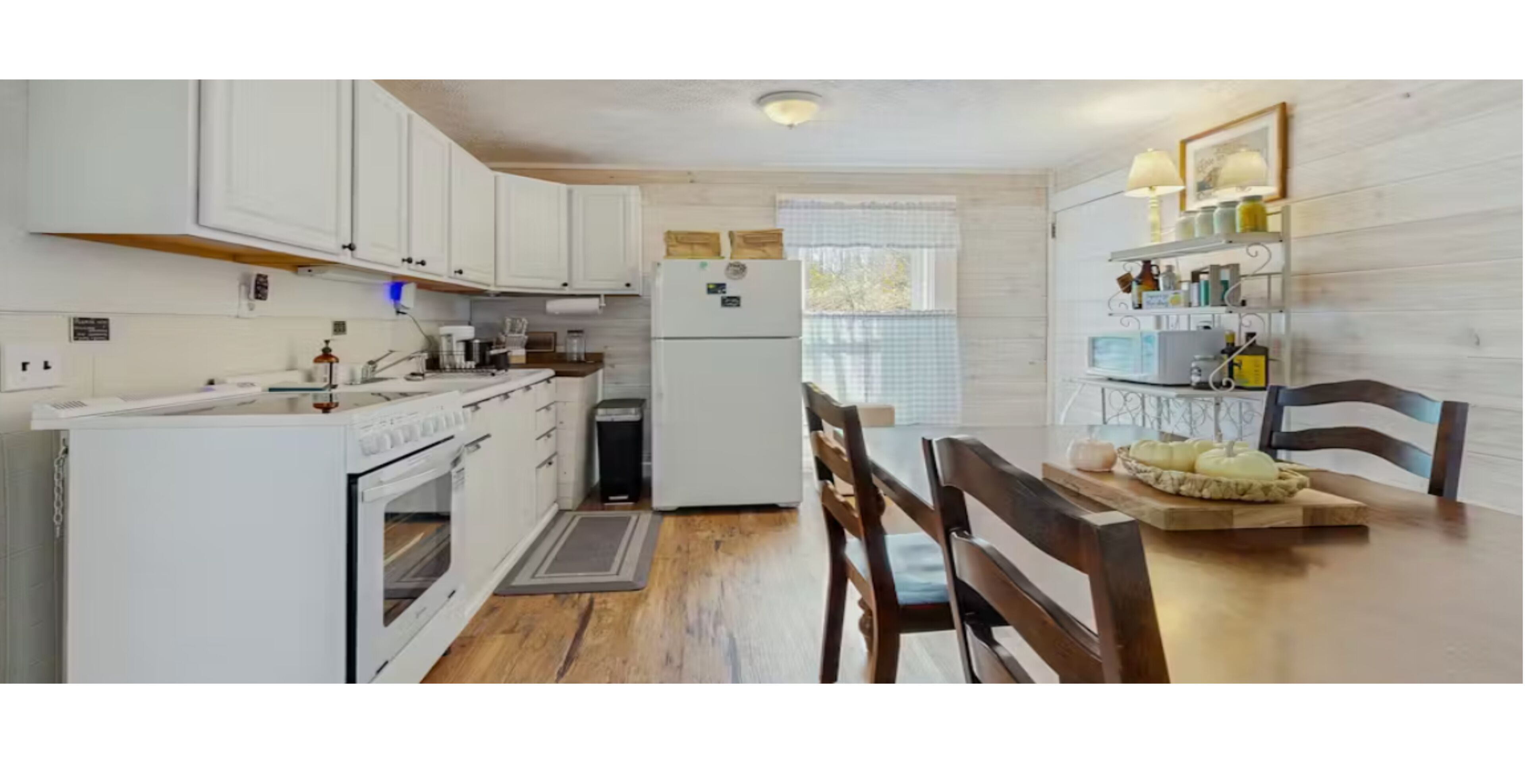 A kitchen with white cabinets, a refrigerator, a stove, and a dining table with chairs.