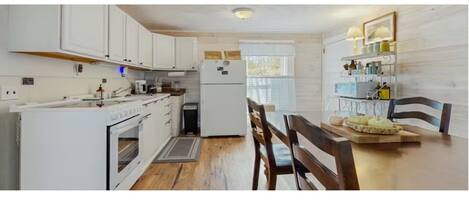 A kitchen with white cabinets, a refrigerator, a stove, and a dining table with chairs.