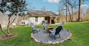 A house with a porch, outdoor seating with chairs and a fire pit, surrounded by a gravel area and grass. - Firefly Cottage, a charming 2-bedroom cabin in Hendersonville, NC (Hendersonville)